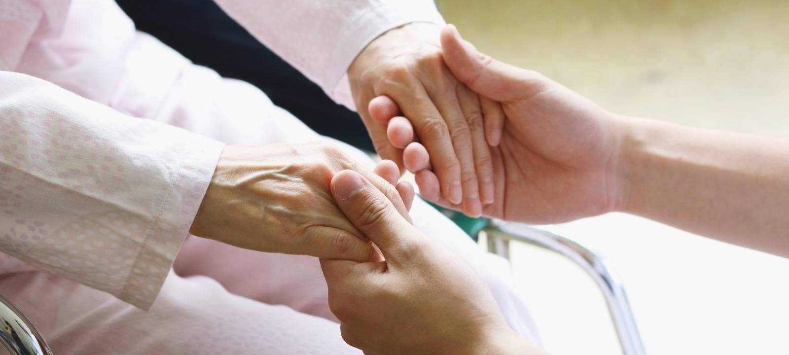 junge Hände eines Pflegers halten die Hände einer alten Dame