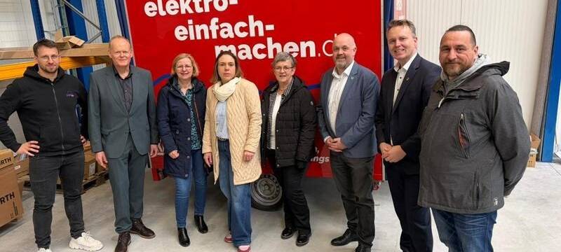 Drei Frauen und fünf Männer vor einem Auto-Anhänger mit roter Plane und der Aufschrift "elektro - einfach - machen".