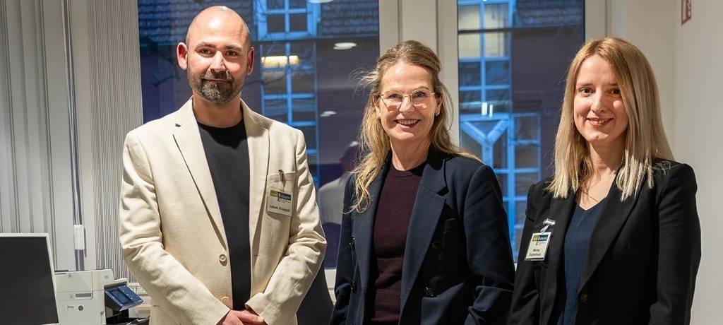 Vertreter der Stadt Münster an einem Computer-Arbeitsplatz - im Vordergrund ein Tisch-Schild mit Aufschrift "Welcome Desk"