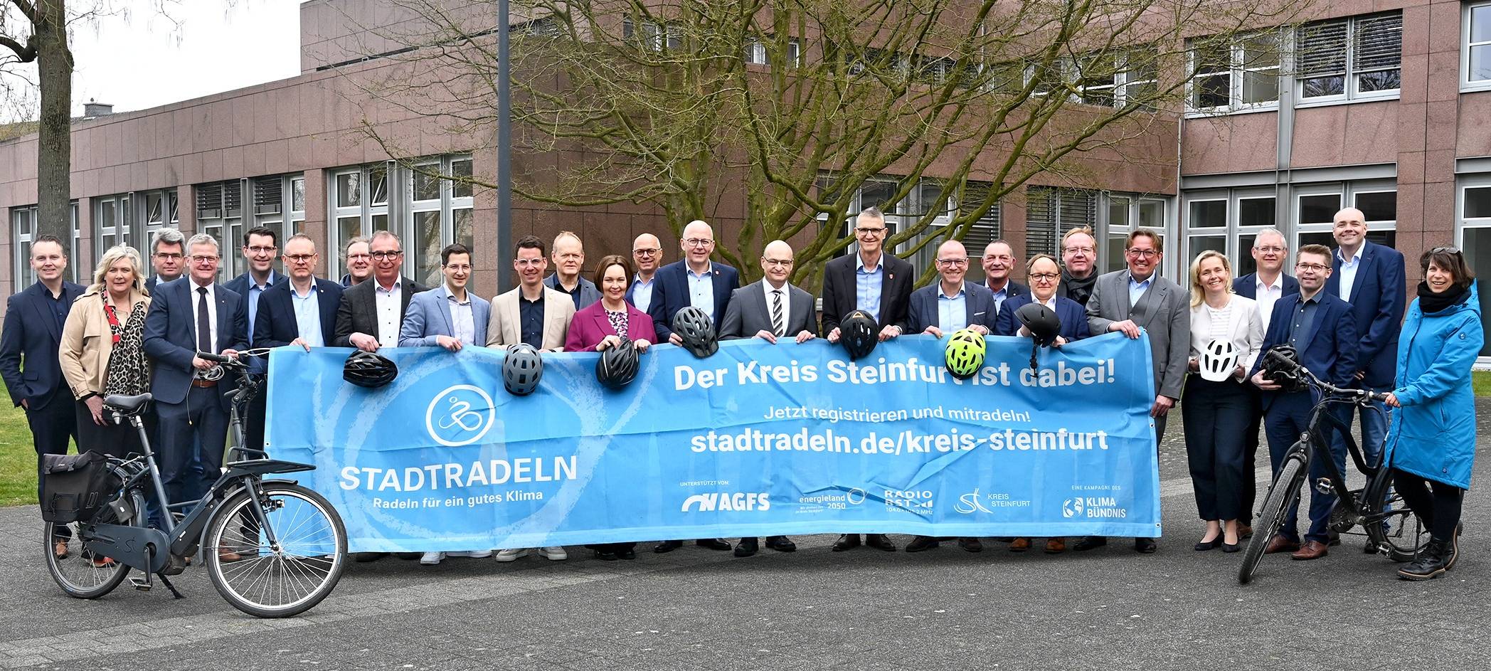 Die Bürgermeisterinnen und Bürgermeister des Kreises Steinfurt halten ein Banner zu der Aktion "Stadtradeln" hoch.