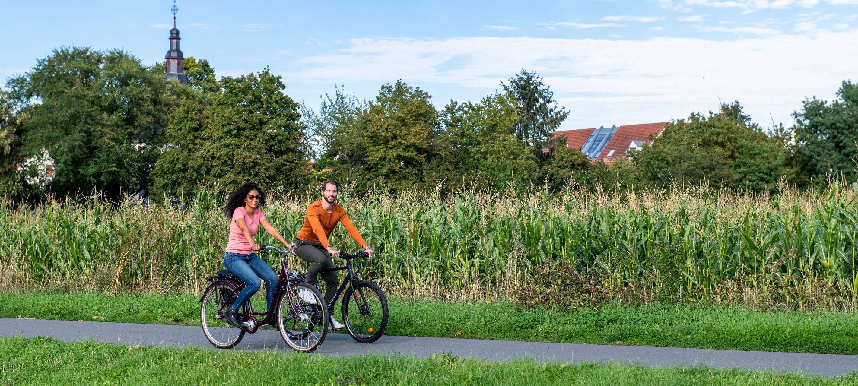 Zwei Menschen fahren auf dem Fahrrad über einen Weg entlang von Feldern.